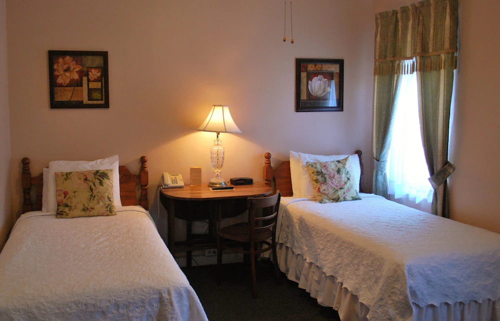 Twin guest room with two beds, floral pillows and an antique desk